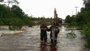 Sertu Budihardjo tampak sedang menggandeng seorang Ibu-ibu, untuk melewati jalan yang terkena banjir.